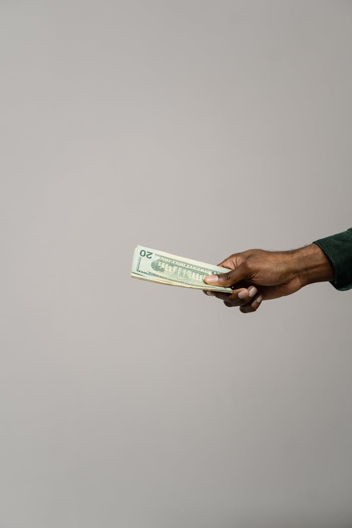 A person holding US twenty dollar bills against a neutral background.